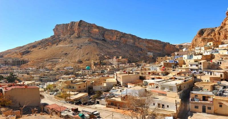 Panoramabild vom Dorf Maaloula in Syrien mit Häusern und massivem Felsen und Gebirge und blauem Himmel